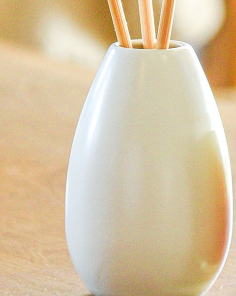 丸みのある白い磁器容器にラタンスティックをさした様子